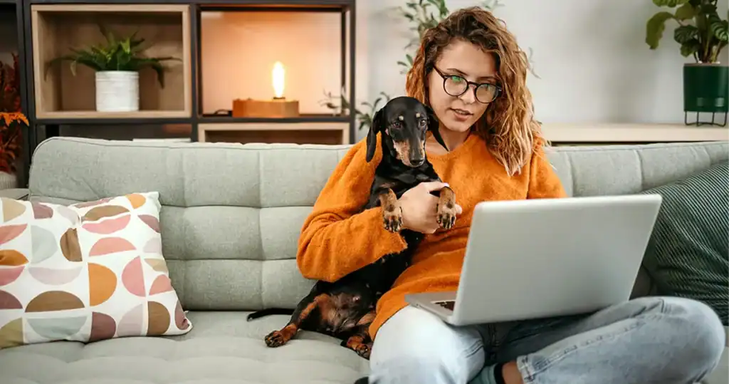 Woman working on laptop with her dog on a cozy sofa.