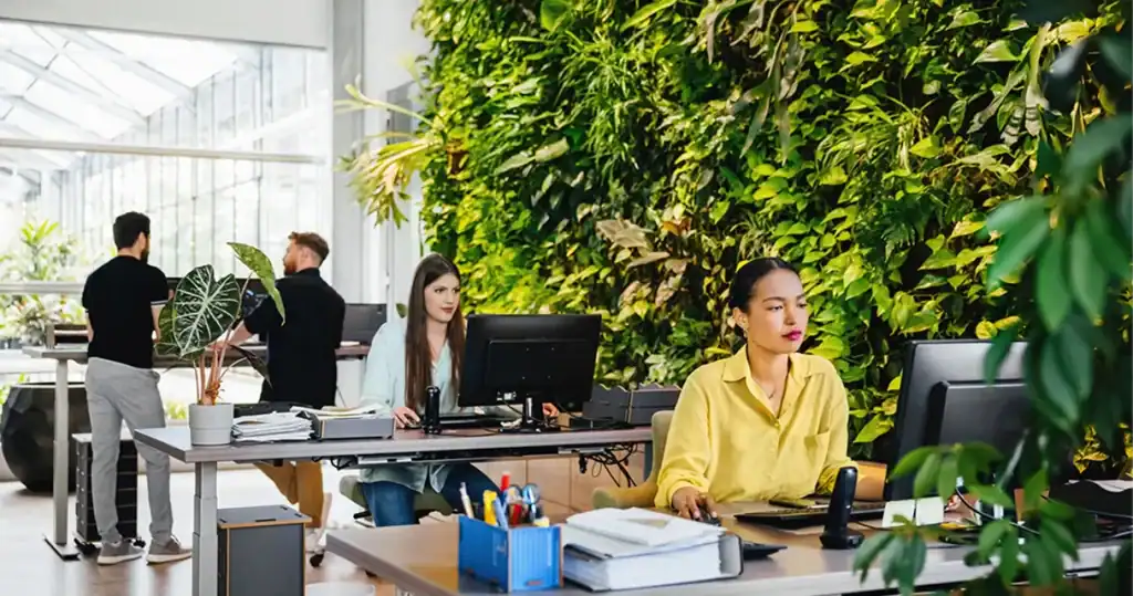 Modern office workspace with a lush green living wall and employees working at desks.
